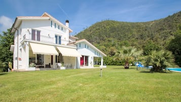 Una casa a due piani con un balcone, una piscina e un prato verde e rigoglioso.