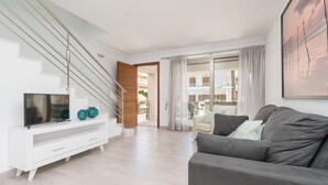 A modern living room with a staircase, a grey sofa, and a flat-screen TV on a white console. - FORMENTERA 1 - Modern terraced house near the beach. Free WiFi (Muro)