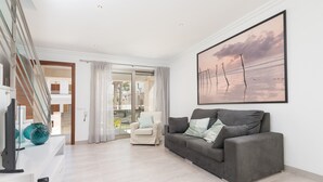 A modern living room with a grey sofa, a white armchair, and a large painting of a beach scene. - FORMENTERA 1 - Modern terraced house near the beach. Free WiFi (Muro)