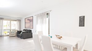 A modern living room with a white dining table, grey sofa, and a large window with sheer curtains. - FORMENTERA 1 - Modern terraced house near the beach. Free WiFi (Muro)