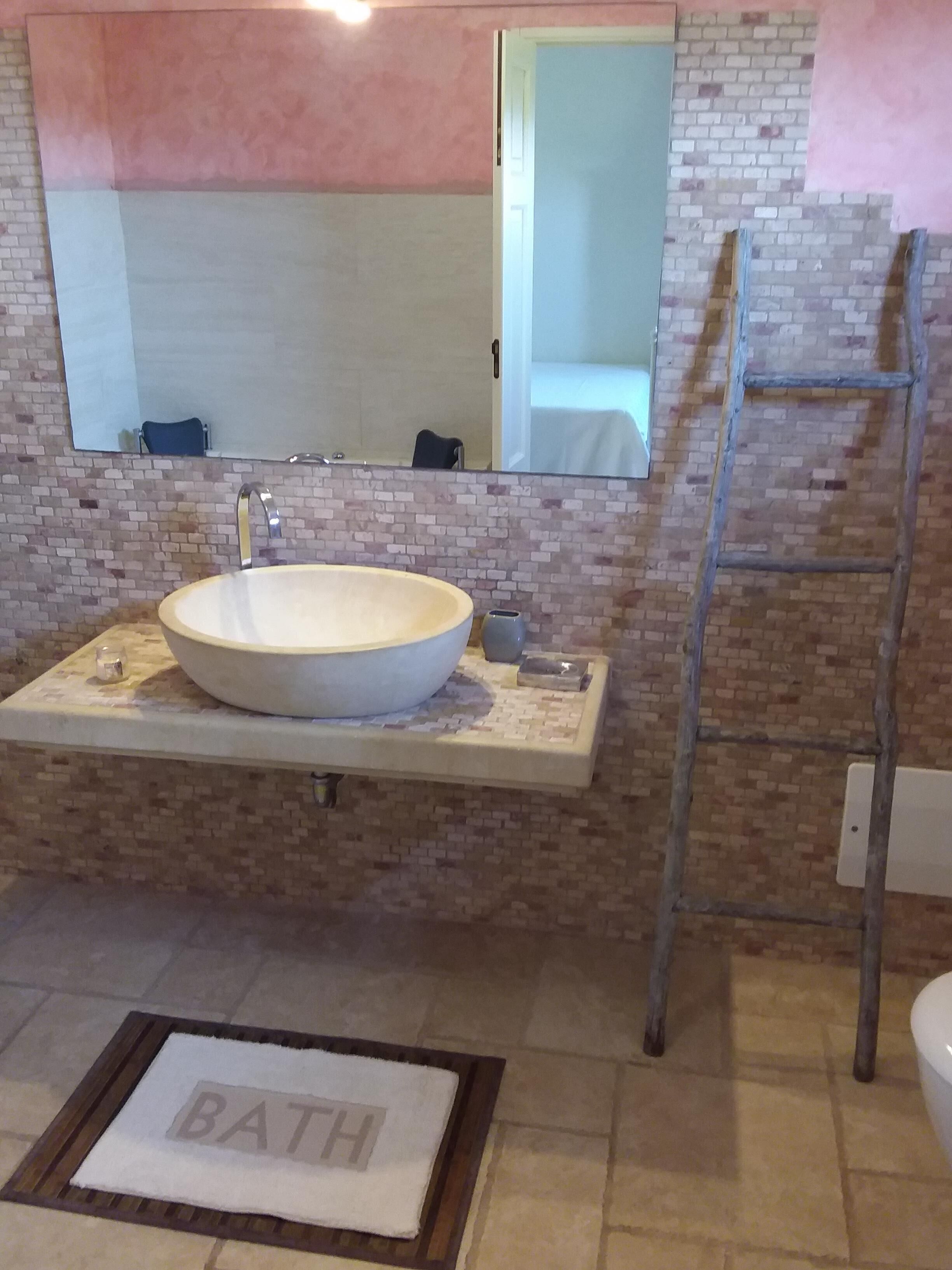 A bathroom with a large round sink, a mirror above it, and a ladder against the wall.