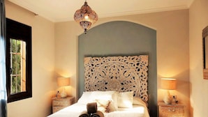 Una camera da letto con una grande testiera decorata, un letto con lenzuola bianche, due lampade da comodino e un lampadario.