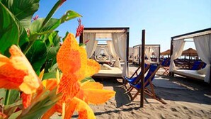 Una spiaggia con tende bianche, poltrone da sdraio azzurre e un fiore tropicale in primo piano.