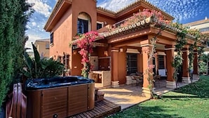 Una casa a due piani con patio, vasca idromassaggio e zona salotto esterna coperta.