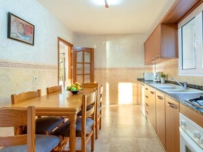 A kitchen with wooden cabinets, a dining table with chairs, and a fruit bowl. - Villa Heura· Villa with private pool in Alcúdia (Alcúdia)
