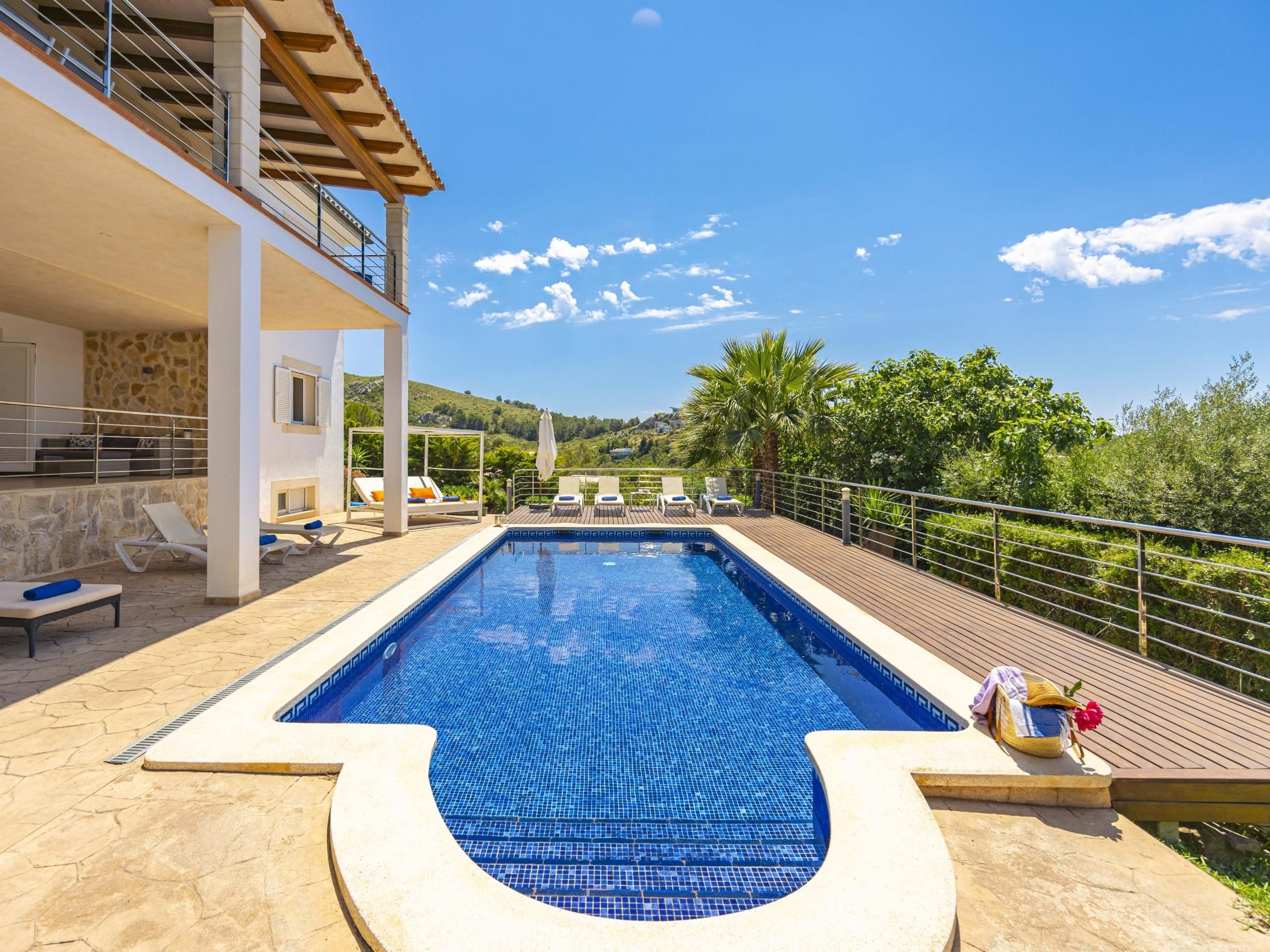 A swimming pool with a view of a hillside, lounge chairs, and a stone wall.