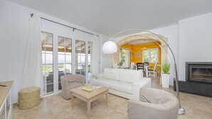 A spacious living room with a white sofa, a wooden coffee table, and a beige armchair. There is a dining area in the background with a table and chairs. - Villa Heura (Alcúdia)