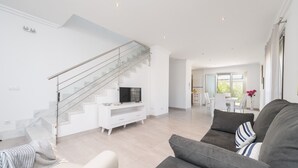En moderne stue med trappe, en grå sofa og et hvidt tv-møbel.