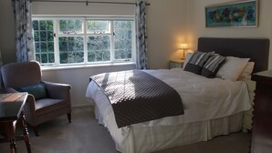 Une chambre à coucher avec un grand lit, une chaise, un bureau, une fenêtre avec des rideaux et un tableau au mur.
