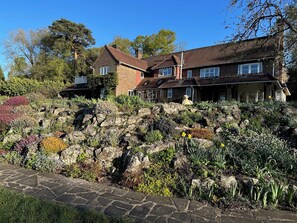 Een groot huis met een pad van stenen dat naar de ingang leidt, omringd door een tuin met diverse planten en bloemen.
