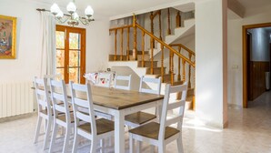 Un coin repas avec une table en bois et des chaises blanches, un escalier et un tableau accroché au mur.