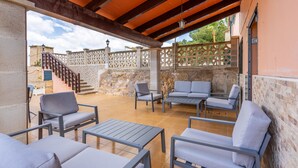 Une terrasse extérieure avec des meubles gris, un mur en pierre et un escalier en bois.
