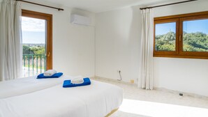 Une chambre d’hôtel avec deux lits, un balcon, une fenêtre donnant sur un beau paysage et un appareil de climatisation.