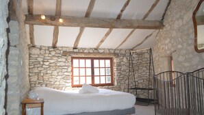 Een slaapkamer met een stenen muur, houten plafond, een bed, een raam en een metalen bedframe.