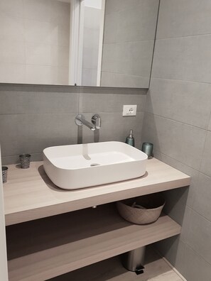 Un baño moderno con un lavamanos blanco, un espejo y un perchero para toallas.