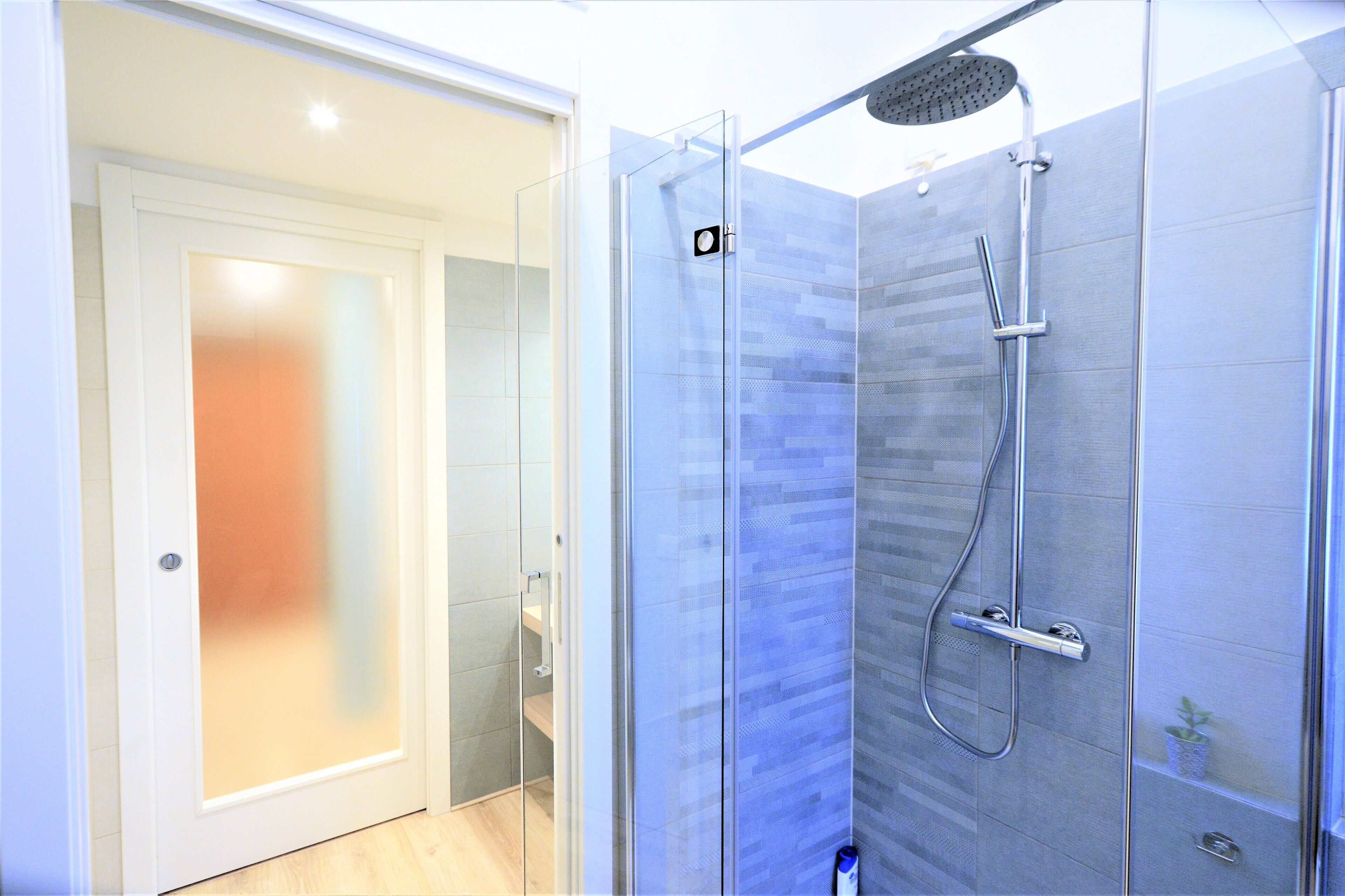 A modern bathroom with a glass shower enclosure, a handheld showerhead, and a wall-mounted faucet.