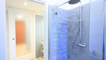 A modern bathroom with a glass shower enclosure, a handheld showerhead, and a wall-mounted faucet.