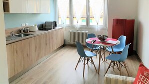Una cocina compacta con fregadero, microondas y armarios. Hay un comedor con mesa y sillas, y una ventana con cortinas.