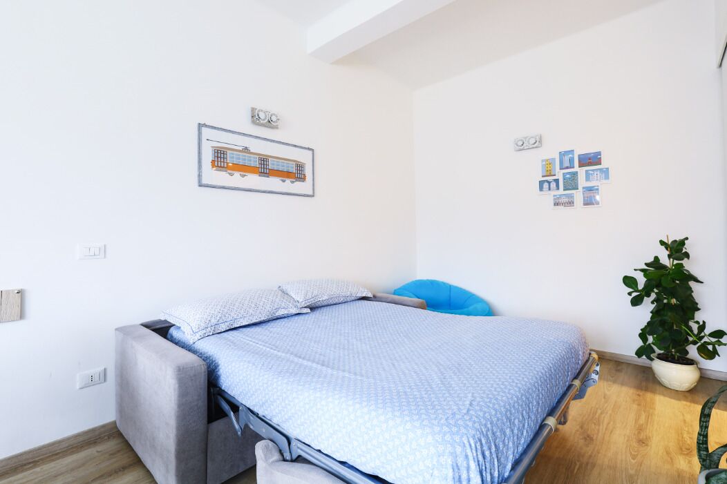 Une chambre à coucher avec un lit, une chaise, une plante et un mur décoré de tableaux et d’une photographie encadrée représentant un train.