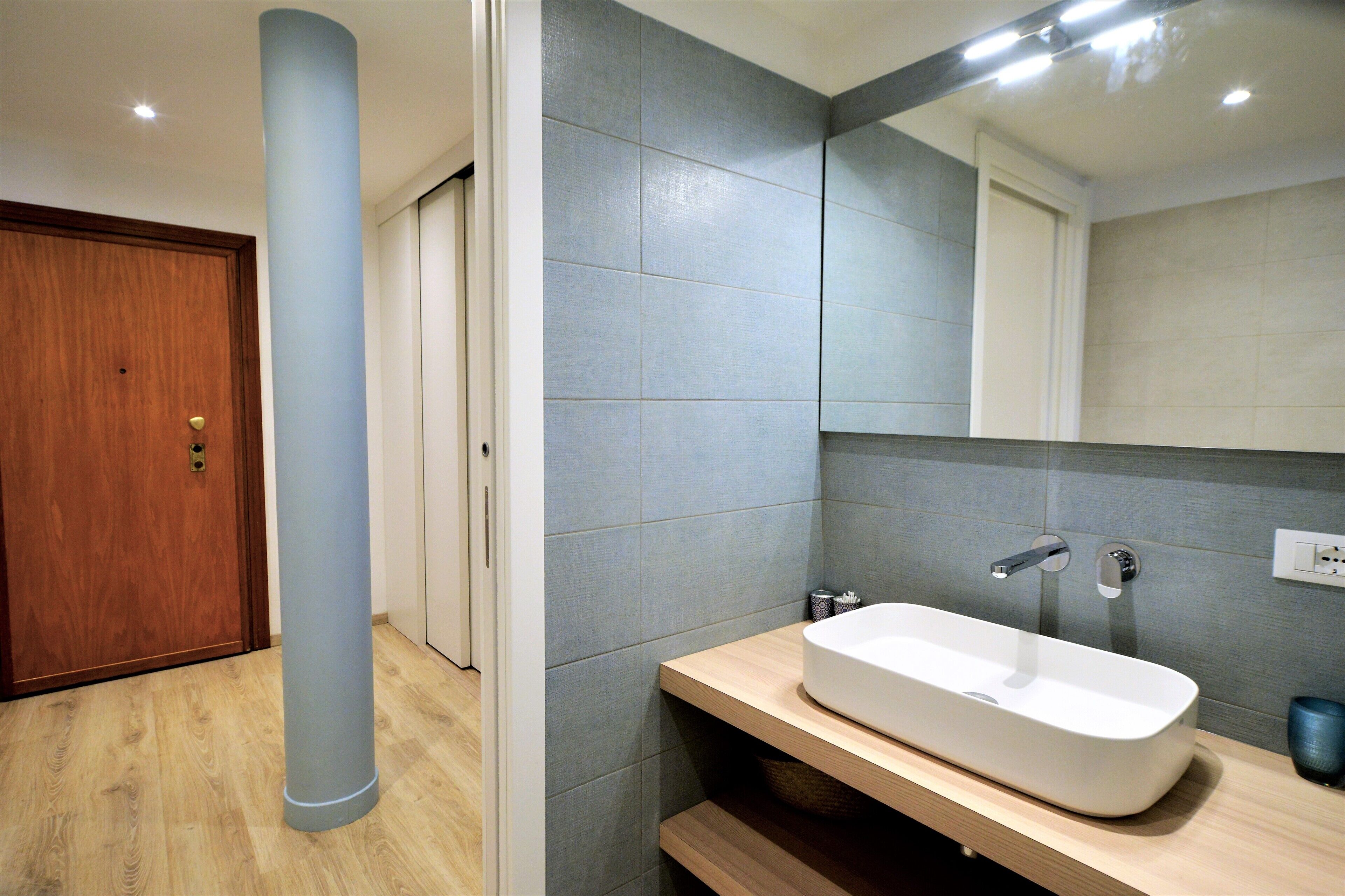 A modern bathroom with a wooden door, a large mirror, and a white sink.