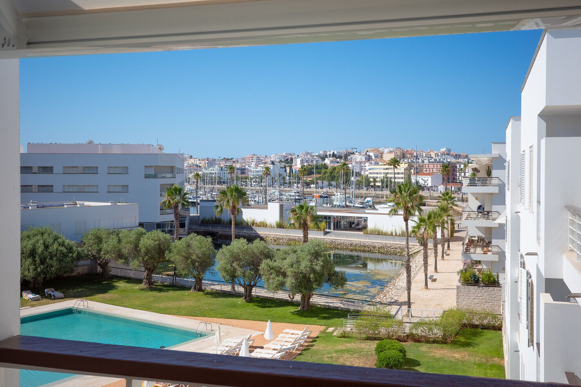 A balcony with a view of a marina, a swimming pool, and surrounding buildings.