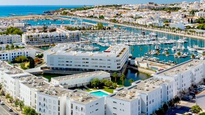 Un port de plaisance abritant de nombreux bateaux, une grande roue et un bâtiment moderne blanc doté d’une piscine sur le toit.