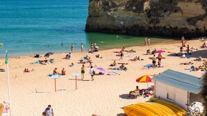 Une plage où des gens se prélassent au soleil et se baignent, une tour de surveillance des sauveteurs et un petit bâtiment avec un toit bleu.