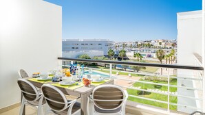 Un balcon avec une table à manger dressée pour le petit-déjeuner, offrant une vue sur un port de plaisance et le paysage urbain.
