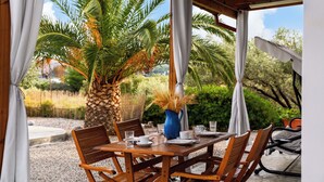 Una mesa de madera lista para comer, con sillas, un florero con plantas secas y vistas a palmeras y follaje.