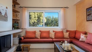 Una sala de estar acogedora con un sofá rojo, una chimenea y un ventanal con vistas a árboles.
