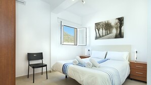 A bedroom with a bed, a chair, a bedside table, a nightstand, and a window. - VILLA BERNAT - 10 MIN WALK TO THE BEACH (Puerto Pollensa)