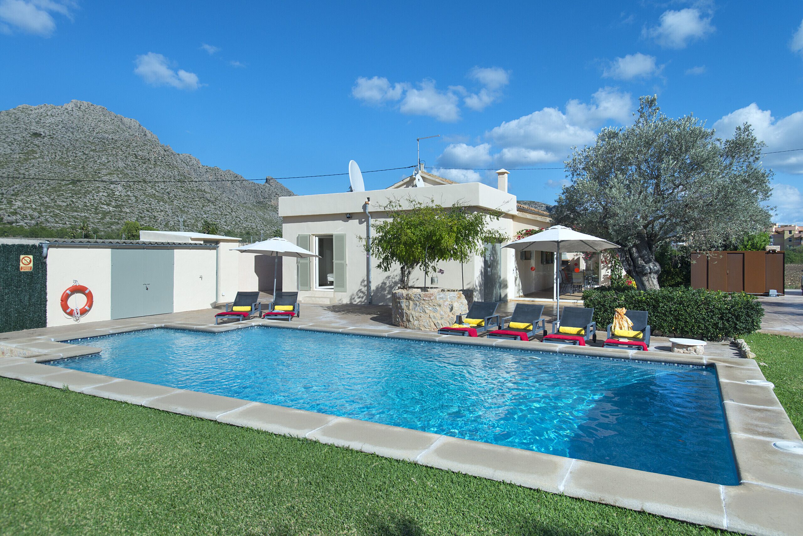 A swimming pool with lounge chairs and umbrellas, surrounded by a well-maintained lawn and a mountain in the background.
