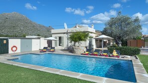 A swimming pool with lounge chairs and umbrellas, surrounded by a well-maintained lawn and a mountain in the background. - VILLA BERNAT - 10 MIN WALK TO THE BEACH (Puerto Pollensa)
