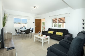 A modern living room with a white coffee table, black sofa, and dining area with chairs.