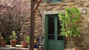 Ein Steinhaus mit einer Holzpergola, grünen Fensterläden und Topfpflanzen.