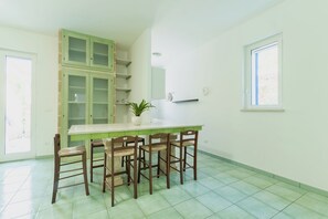 Une cuisine avec un meuble vert, un plan de travail blanc et quatre chaises en bois.