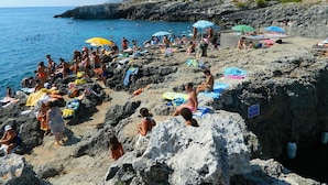 Une plage rocheuse où des gens se prélassent au soleil et se baignent.