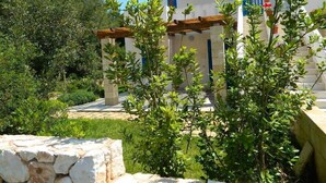 Un bâtiment de style méditerranéen traditionnel, doté d’un mur en pierre, d’une pergola en bois et d’une végétation luxuriante.