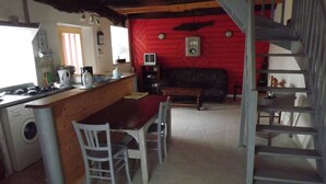 A kitchen with a wooden counter, a dining area with a red sofa, and a staircase. - Breton house 2 bedrooms bathroom / living room / kitchen (Ploezal)