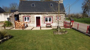 A stone house with a red door, a small porch, and a fenced yard. - Breton house 2 bedrooms bathroom / living room / kitchen (Ploezal)