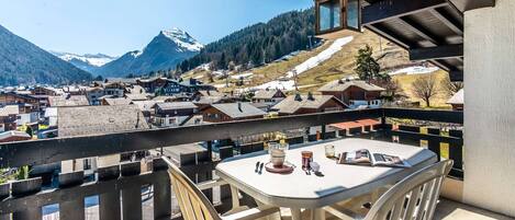 A balcony with a table and chairs overlooking a mountainous village.