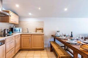 A modern kitchen with wooden cabinets, a stainless steel range hood, a microwave, and a dining table set for a meal. - Luxurious penthouse 3 bed in the center (MORZINE)