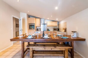 A dining area with a wooden table set for four, equipped with a microwave, oven, and a scale.