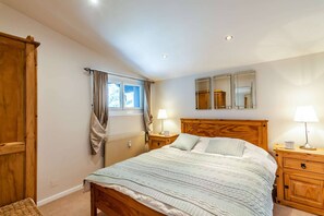 A bedroom with a wooden bed, two bedside tables with lamps, a window with curtains, a radiator, and a mirror on the wall. - Luxurious penthouse 3 bed in the center (MORZINE)