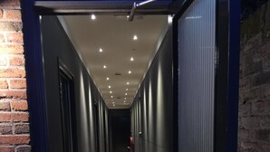 Un couloir doté d’un sol recouvert de moquette, de portes métalliques et d’un mur en briques sur un de ses côtés.