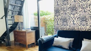 Un salon avec un canapé bleu, une commode en bois et un papier peint à motifs.
