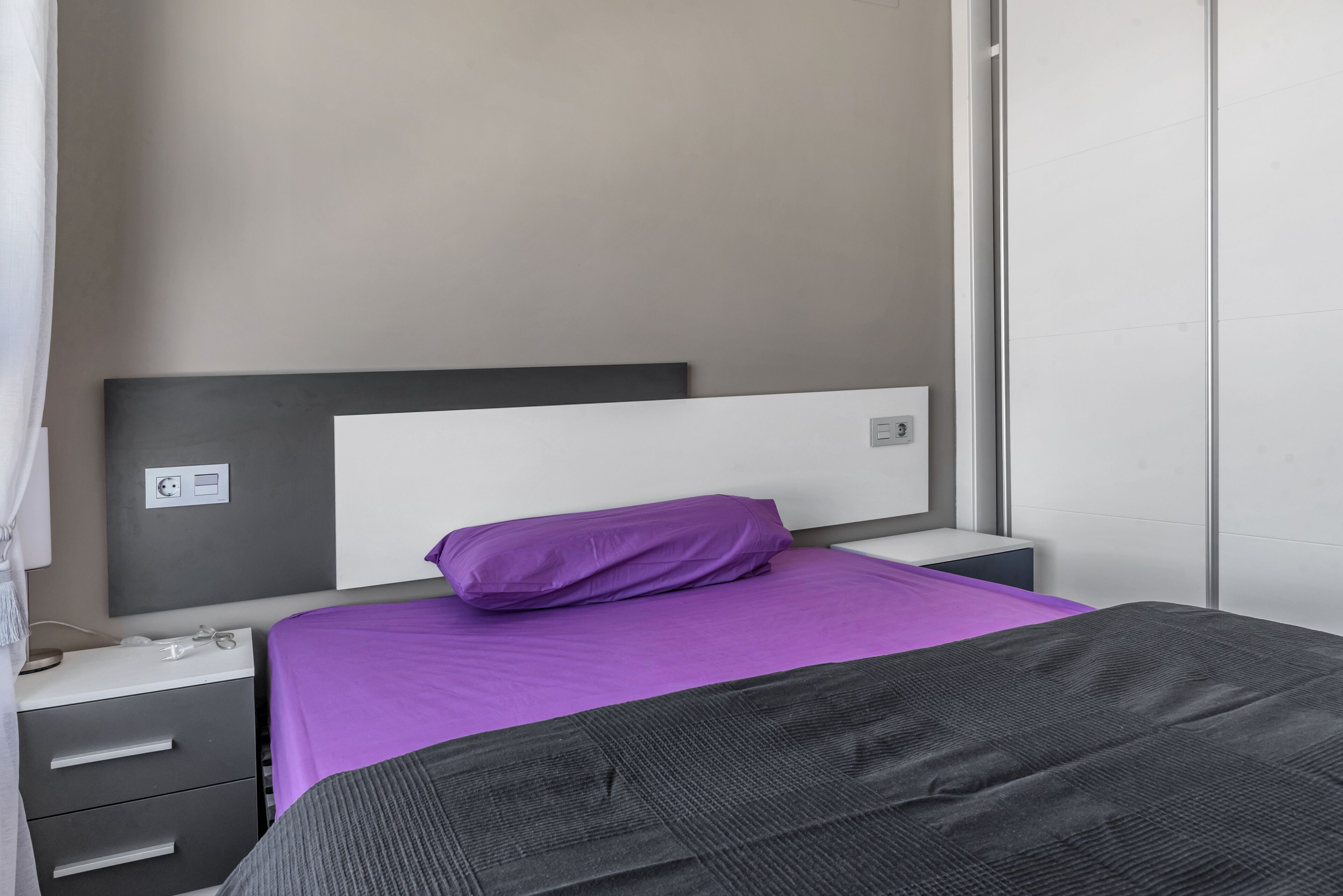 Une chambre à coucher comprenant un lit, une table de chevet, une commode et un interrupteur fixé au mur.