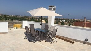 Un patio al aire libre con una mesa, sillas y un paraguas grande, con vistas a la ciudad.
