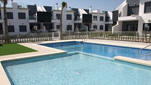 Una piscina rectangular con agua azul cristalina, rodeada por un solárium blanco y una valla baja.