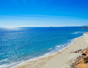 A beach with clear blue water, sandy shore, and distant mountains.